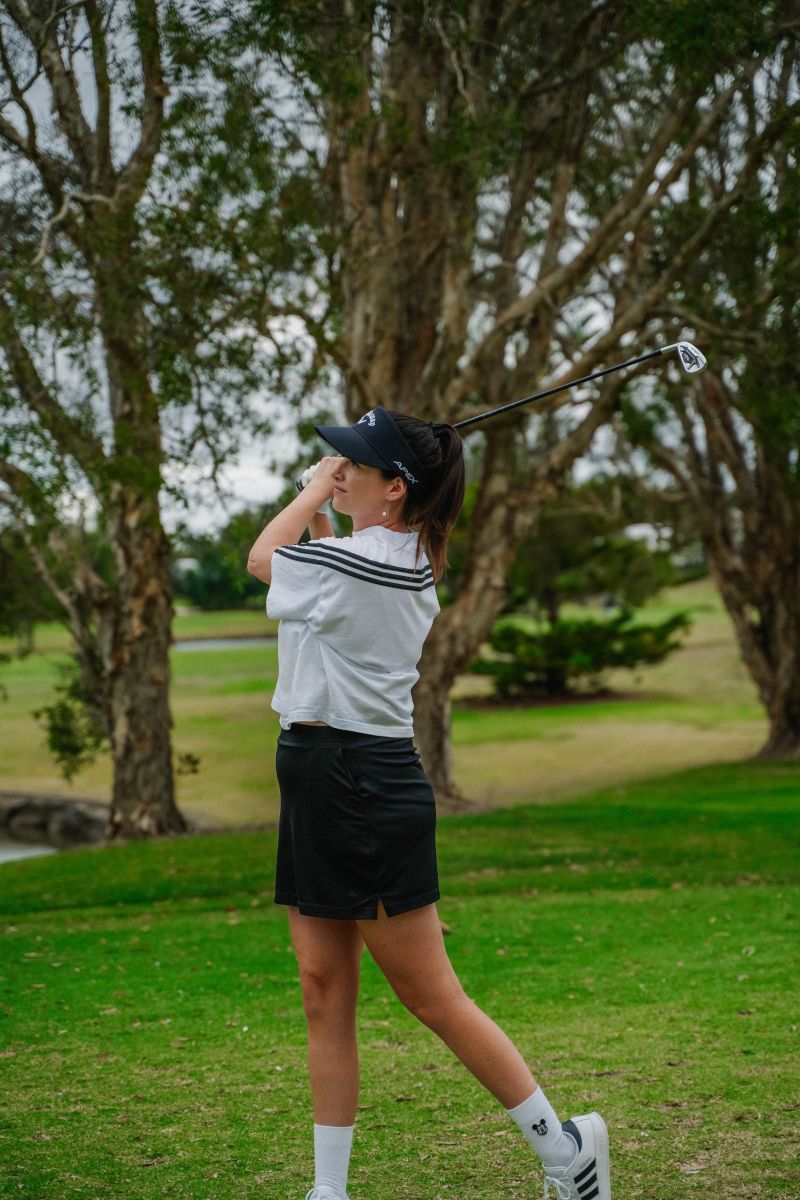 Golfer holding her follow-through under the paperbarks